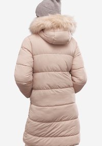 Jasnoróżowa kurtka puchowa z poziomymi przeszyciami, kapturem wykończonym sztucznym futrem i zwężoną w talii fasonem. Noszona z szarym dzianinowym beanie.