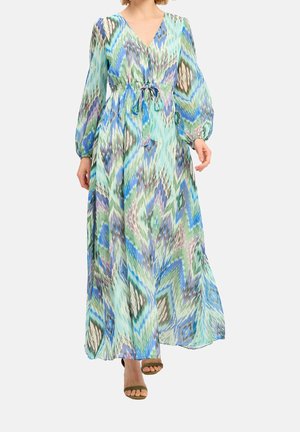 Frau trägt ein langärmeliges Maxikleid mit V-Ausschnitt, versehen mit einem abstrakten Zickzackmuster in Blau, Grün und Lila sowie einem gebundenen Taillengürtel.
