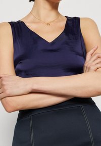 Mörkblå satinärmlös topp med V-ringning och en lätt lyster, ihop med en svart kjol med vita sömdekorationer.