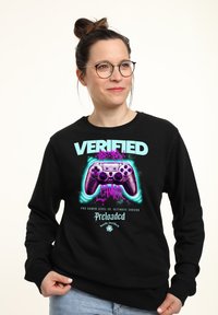 Felpa nera con design grafico colorato che presenta il testo "VERIFIED GAMER" e un'illustrazione di un controller di gioco nei toni del viola.