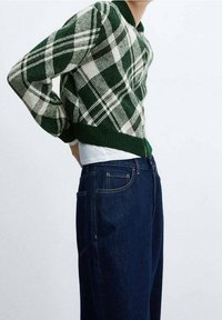 Pull tricoté à carreaux verts et blancs avec un col côtelé, associé à un jean en denim bleu foncé, présentant une coupe décontractée et des poches avant.