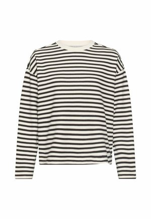 Kvinde står iført sorte jeans med høj talje, sort-hvidstribet langærmet top og hvide sneakers mod en ensfarvet baggrund.