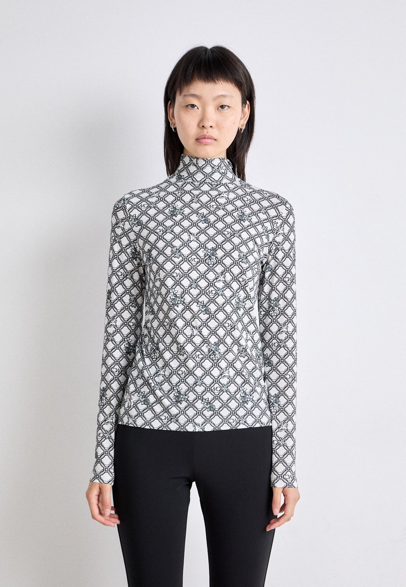 Langärmliges, Stehkragenoberteil in Weiß mit einem schwarzen geometrischen Muster. Glattes, dehnbares Material; figurbetonte Silhouette; kombiniert mit schwarzen Leggings.