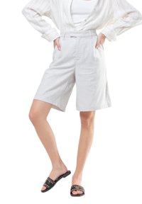 Pantaloni corti in lino grigio chiaro con una vestibilità comoda, lunghezza al ginocchio, con pieghe sul davanti e tasche laterali, abbinati a sandali neri con borchie.