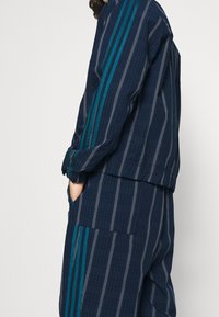 Mörkblå randig träningsdräkt i mjukt tyg, med teal-färgade detaljer och vita pinstripes, samt elastiska mudd och fickor.