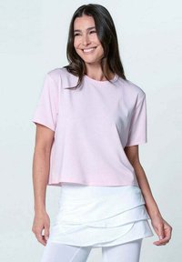 T-shirt cropped rosa chiaro con maniche corte, realizzato in tessuto liscio. Indossato con una gonna bianca a strati, su uno sfondo neutro.