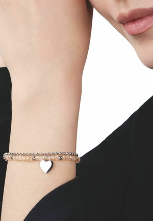 Brazo con dos pulseras de cuentas, una con cuentas color durazno y un dije de corazón plateado, la otra con pequeñas cuentas plateadas, sobre una manga negra.