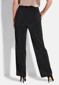 Pantalons larges noirs avec une texture scintillante. Dotés de poches ; taille haute, associés à des talons aiguilles. Taille élastique subtile.