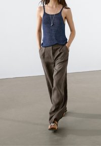 Casuele outfit met een marineblauwe gebreide tanktop en losse, taupe broek met een gladde textuur en geplooide voorkant. Sandalen maken de look compleet.