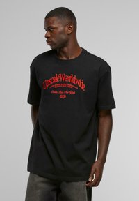 Black cotton t-shirt with short sleeves. Features red printed text reading "Upscale Worldwide" and additional branding. Classic fit design.