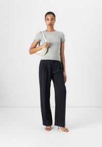 Maglietta grigia aderente, pantaloni larghi blu navy e una borsa a tracolla bianca. La modella è in piedi contro uno sfondo semplice, indossando sandali con cinturini.
