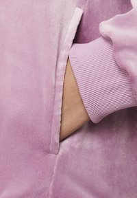 Svijetloplava velur kapuljača s kengurujim džepom i rebrastim manžetama, mekanog, plišanog tekstura i glatkim, sjajnim završetkom.