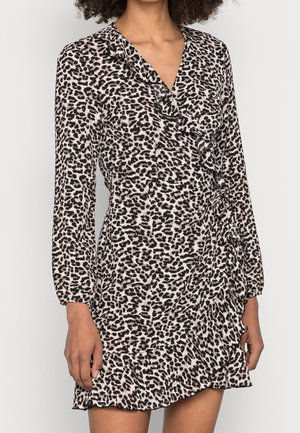 Kobieta w długim rękawie, V-dekoltem, zwierzęcym wzorem, sukience kopertowej z falbankami wzdłuż dołu i zapięcia na przodzie.