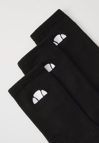 Drei schwarze gerippte Socken mit weißen, croissantförmigen Logos auf weißem Hintergrund, diagonal überlappt angeordnet.