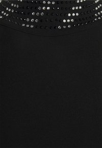 Peça de vestuário preta com uma textura suave e um decote adornado com filas de strass claros e pretos.