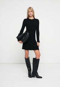 Abito a maglia nero a coste con maniche lunghe, lungo fino al ginocchio. Abbinato a una borsa nera elegante e morbida e stivali neri con tacco fino al polpaccio.