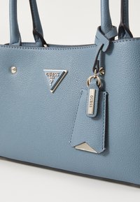 Borsa a tracolla blu con texture, dotata di hardware dorato, logo triangolare e etichetta pendente. Presenta manici robusti e una superficie inferiore liscia.