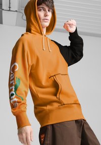 Felpa con cappuccio di colore arancione davanti e maniche nere, dotata di tasca a marsupio e logo "Carrots" in bianco e verde.