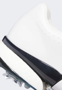 Bílá sportovní bota s hladkým svrškem, tmavě modrými akcenty, strukturovanou stélkou a průhlednou podrážkou s hroty pro lepší přilnavost.