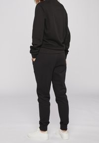 Černá mikina s dlouhými rukávy a žebrovanými manžetami, doplněná o odpovídající zúžené tepláky. Oblečení má volný střih a měkkou texturu.