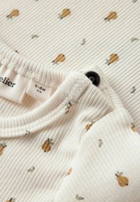 Top di tessuto bianco a coste con piccole stampe di pere marroni e foglie verdi, con chiusura a scatto e un'etichetta che indica la taglia 2-4 mesi.