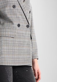 Blazer doppio petto grigio a quadri con bottoni neri, caratterizzato da una vestibilità su misura, revers a punte e taschino sul petto. Tessuto testurizzato.
