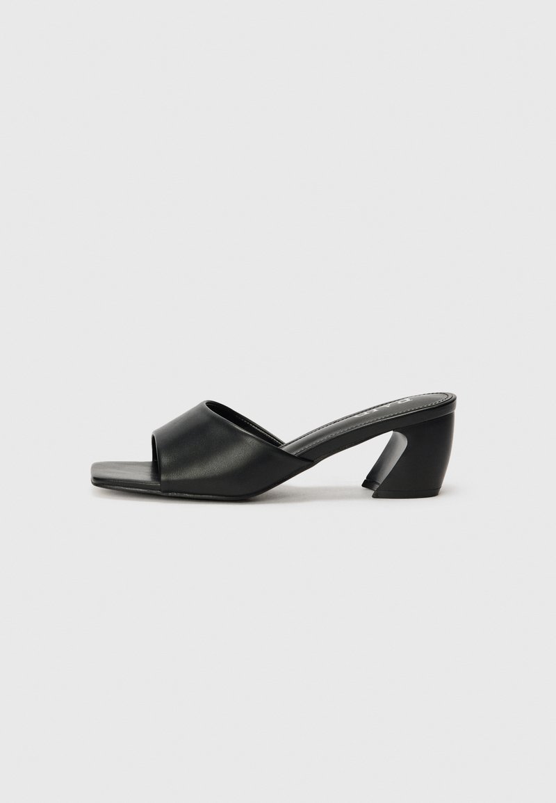 Schwarze High Heelsandale mit einem glatten Obermaterial aus Kunstleder, offenem Zehendesign und einem markanten, kantigen Absatz. Minimalistische, quadratisch geformte Fußbetten.