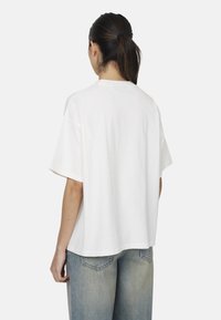 T-shirt bianco in cotone con maniche corte, vestibilità rilassata e scollatura rotonda, mostrato da dietro. Abbinato a jeans azzurri chiari.
