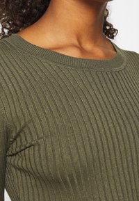 Pull côtelé vert olive avec un col rond, un tissu texturé et une coupe ajustée mettant en valeur les fines lignes verticales.