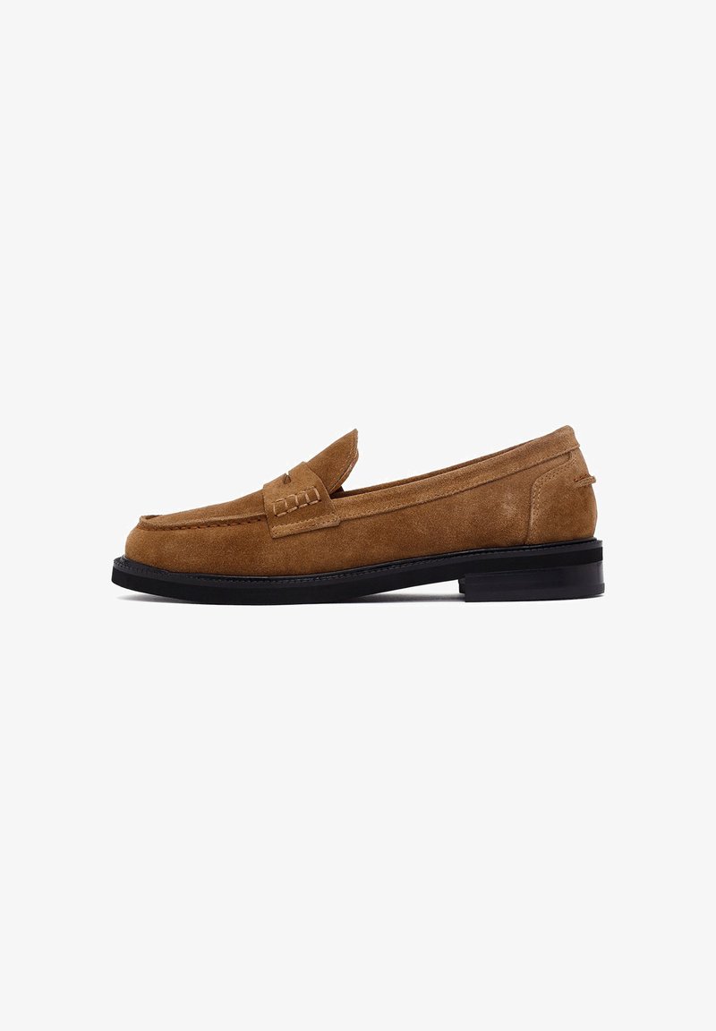 Mocassini in suede marrone con suola nera bassa, dettagli cuciti sulla parte anteriore del piede e design slip-on classico.