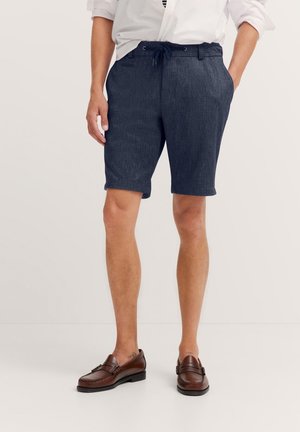 Navy blue shorts made of textured fabric, featuring drawstring closure and side pockets, paired with brown leather loafers.