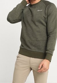 Felpa verde con texture, collo rotondo, polsini e orlo a coste. Presenta un piccolo logo bianco sul petto e un design dalla vestibilità rilassata.