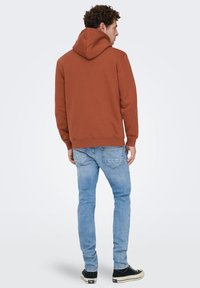 Bruine capuchontrui, gemaakt van een katoenmix, met lange mouwen, een kangoeroezak, een losse pasvorm, gecombineerd met lichtblauwe spijkerbroek en zwarte sneakers.