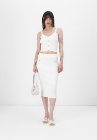 Hvit ribbet to-delt antrekk med en cropped tanktop med frontknapper og et knelangt skjørt med dekorative knapper. Minimalistisk design.