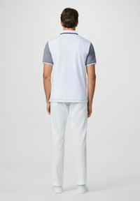 Camisa polo blanca con mangas grises, ajuste slim y ribete en contraste; combinada con pantalones blancos y calzado a juego. Diseño minimalista.