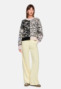Gestrickter Pullover in Schwarz und Beige mit Tigerstreifenmuster, kombiniert mit cremefarbenen, weit geschnittenen Hosen. Strukturierter Strick mit gerippten Bündchen.