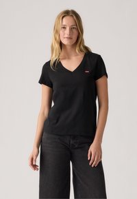 Schwarzes V-Ausschnitt-T-Shirt aus Baumwolle, mit kurzen Ärmeln und einem kleinen roten Markenlogo auf der linken Brust. Glatte Textur, lässiger Schnitt.