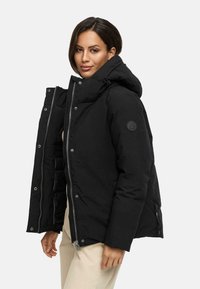 Black puffer jacket with a hood, featuring a front zipper, snap buttons, and a logo patch on the sleeve. Smooth, insulated fabric.