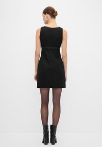 Abito nero senza maniche con tessuto testurizzato, silhouette aderente e chiusura sul retro con cerniera. Accentuato con dettagli di design in vita.