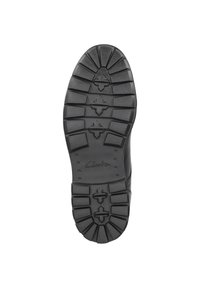 Semelle de chaussure en caoutchouc noir avec des rainures profondes et des motifs de traction ; arbore le nom de la marque "Clarks" en relief près du talon.