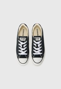Černé plátěné tenisky s bílými tkaničkami, gumovou špičkou a kontrastním bílým štepováním. Na jazyku se nachází logo "Converse All Star".