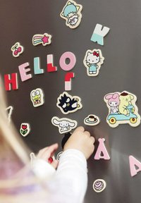 Wooden magnets of letters and cartoon characters in various colors attached to a magnetic surface, with a hand reaching for a piece.