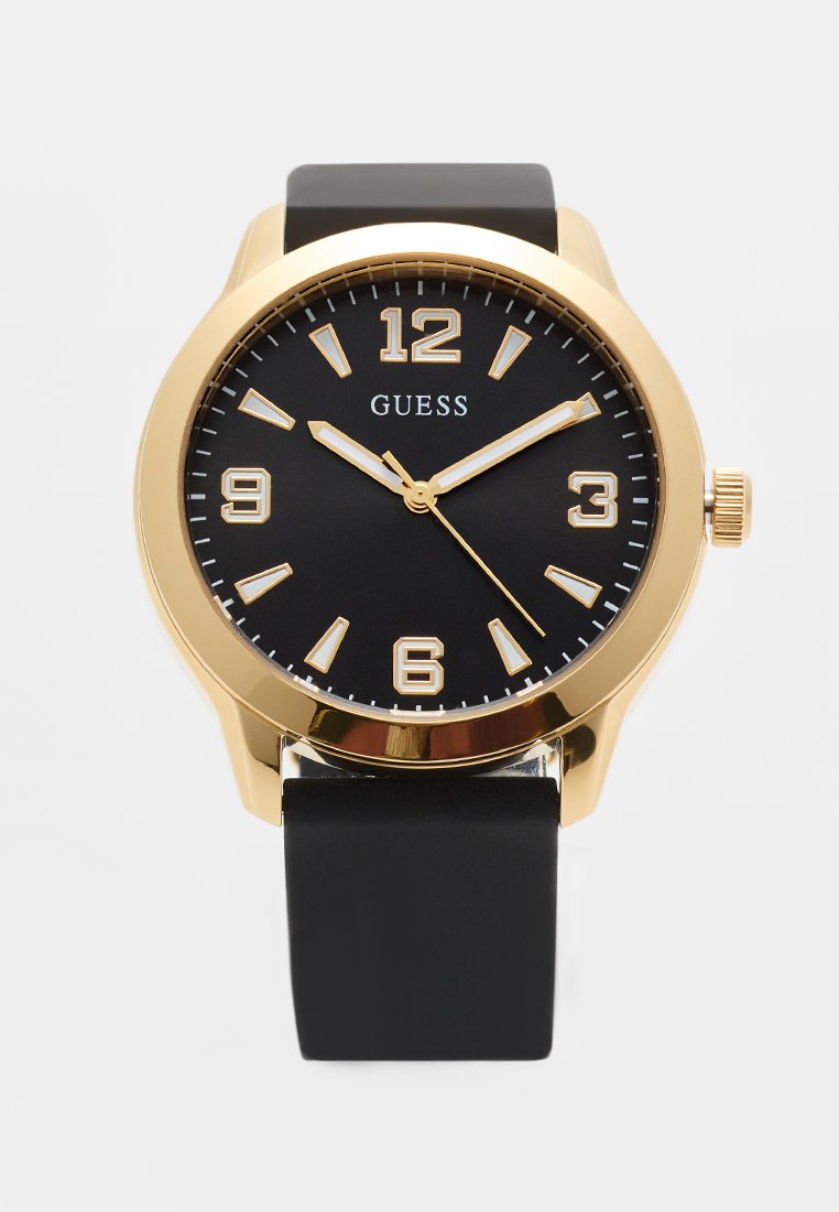 Reloj Guess redondo en tono dorado con esfera negra, marcadores de horas dorados y correa de silicona negra que muestra la hora 10:10:27.