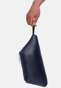 Marineblauwe opbergzak, vastgehouden door een hand, met een soepele textuur, een rits aan één zijde en een zwarte stoffen lus om te dragen.