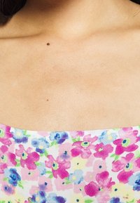 Tissu à imprimé floral dans des couleurs pastel présentant des fleurs roses, bleues et vertes. Encolure carrée avec une texture lisse, mettant en valeur la zone de la poitrine.