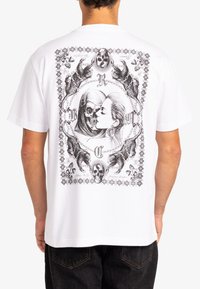 White cotton t-shirt featuring a black printed design of a skull, a woman’s face, and animal motifs framed with decorative borders.