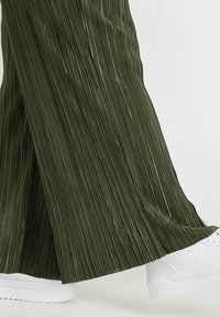 Gröna plisserade vida byxor med en glänsande yta, kombinerade med vita sneakers med en slät yta och synliga snörningar.