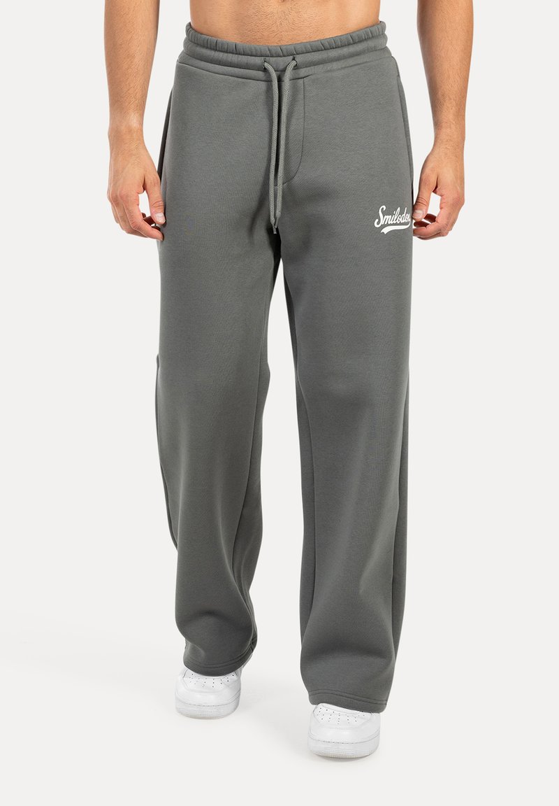 Pantalones de chándal gris claro, hechos de un tejido suave, con cintura ajustable y bolsillos laterales. Decorados con un logotipo de texto blanco en el muslo izquierdo.