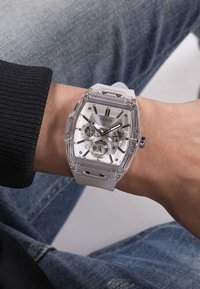 Orologio trasparente con cinturino in gomma bianca, dettagli in argento, marcatori neri delle ore e un quadrante secondario rotondo, indossato su un polso.