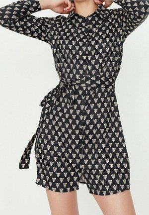 Zwart overhemdjurk met een bloemenprint in crème, lange mouwen, een kraag, knopen aan de voorkant en een ceintuurelement in de taille. Gladde stoftextuur.